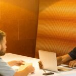 man sitting on black leather bench holding gray laptop computer on top of white wooden table